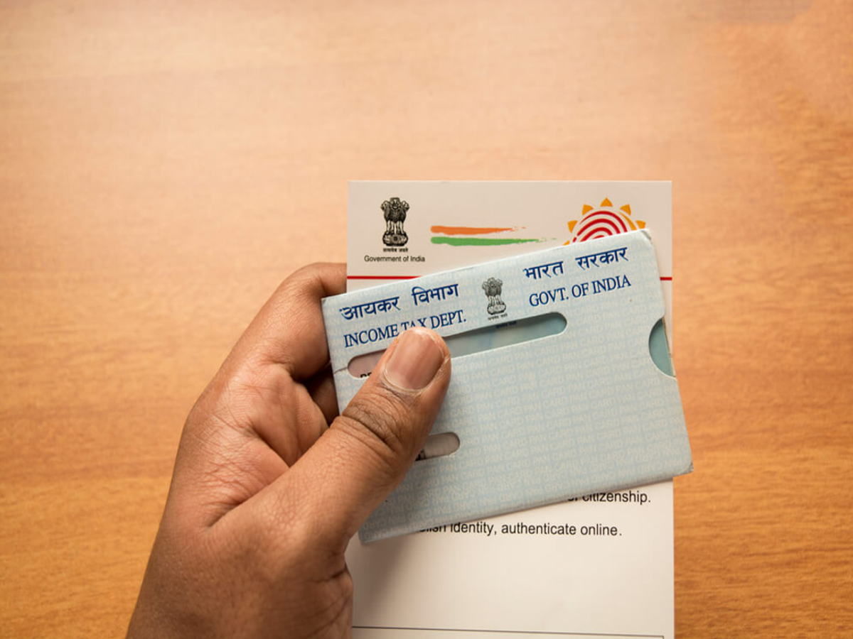 Person holding Aadhaar and PAN cards with a laptop in the background for linking process.